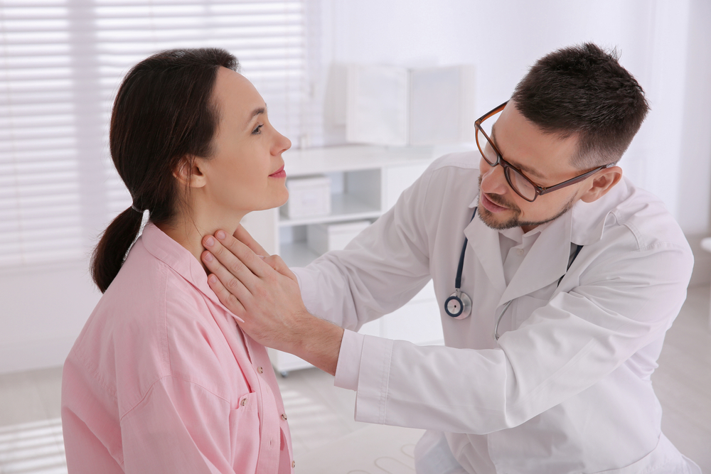 Thyroid surgeon palpating a patient's neck during a clinical examination in a bright medical office